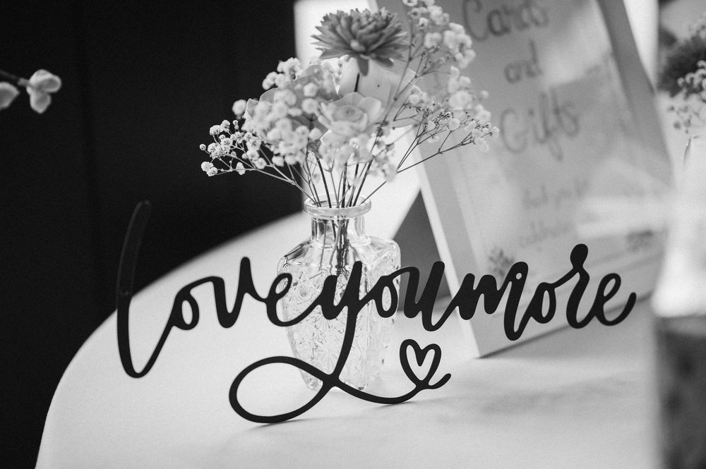 Black and white image showing handwritten text 'Love you more' with delicate baby's breath flowers in a vase.