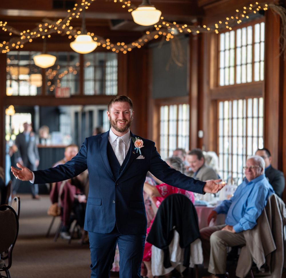 Wedding guests fill a rustic reception venue decorated with string lights while someone makes a grand gesture during the celebration.