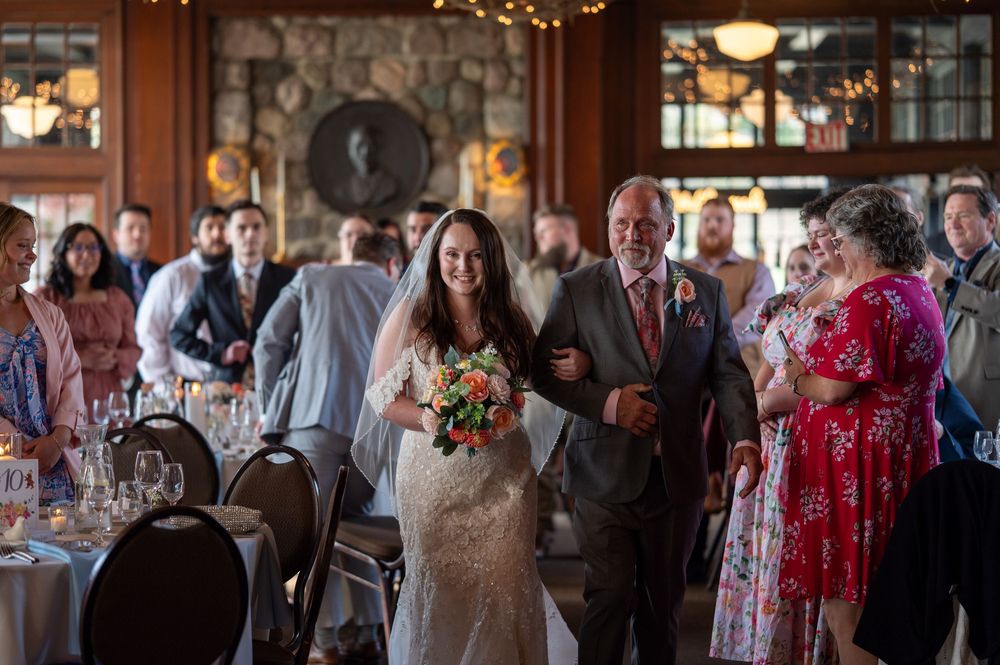 A wedding procession in a rustic lodge venue with stone fireplace and warm lighting during the ceremony.
