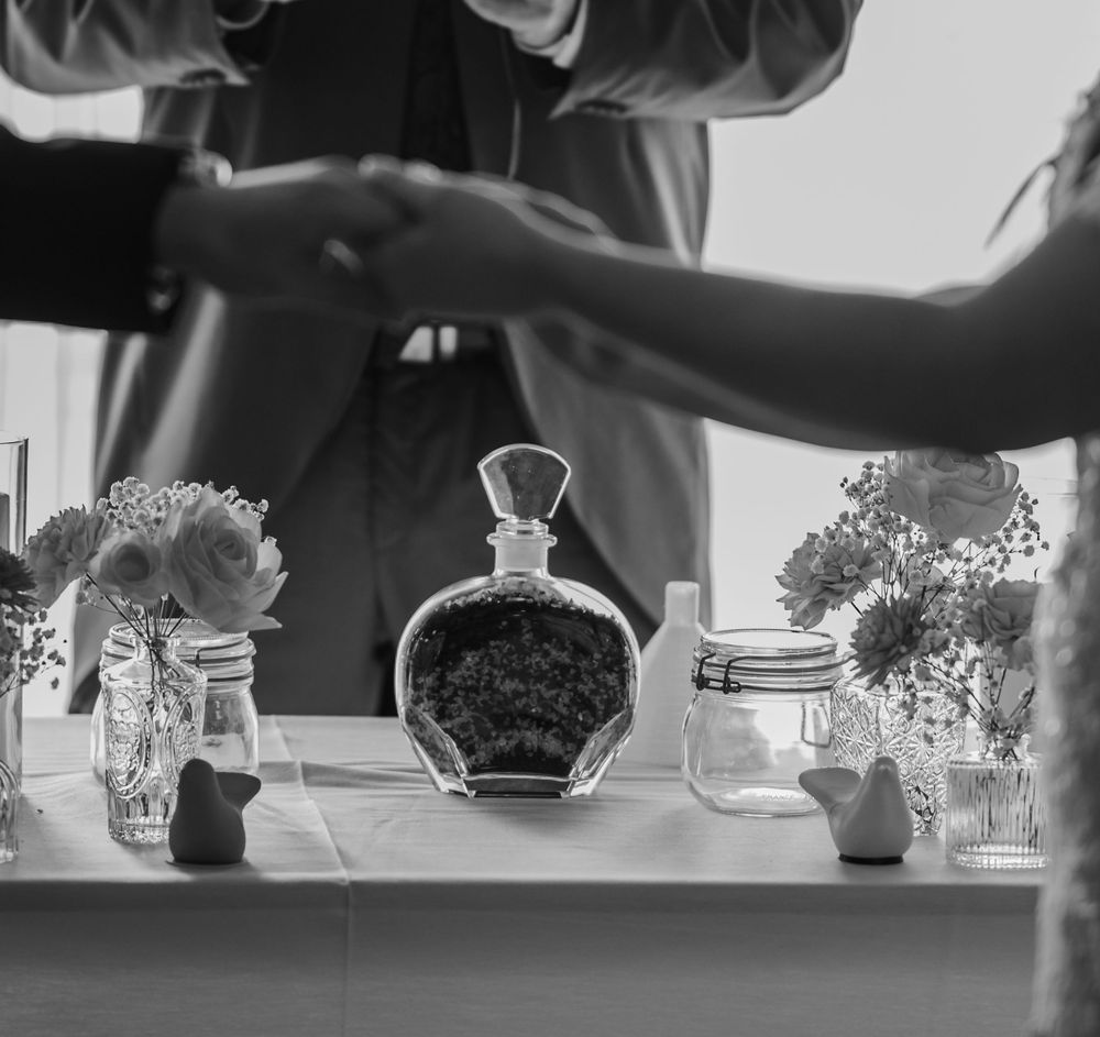 Black and white image of decorative glass bottles and vases with flowers arranged on a table surface.
