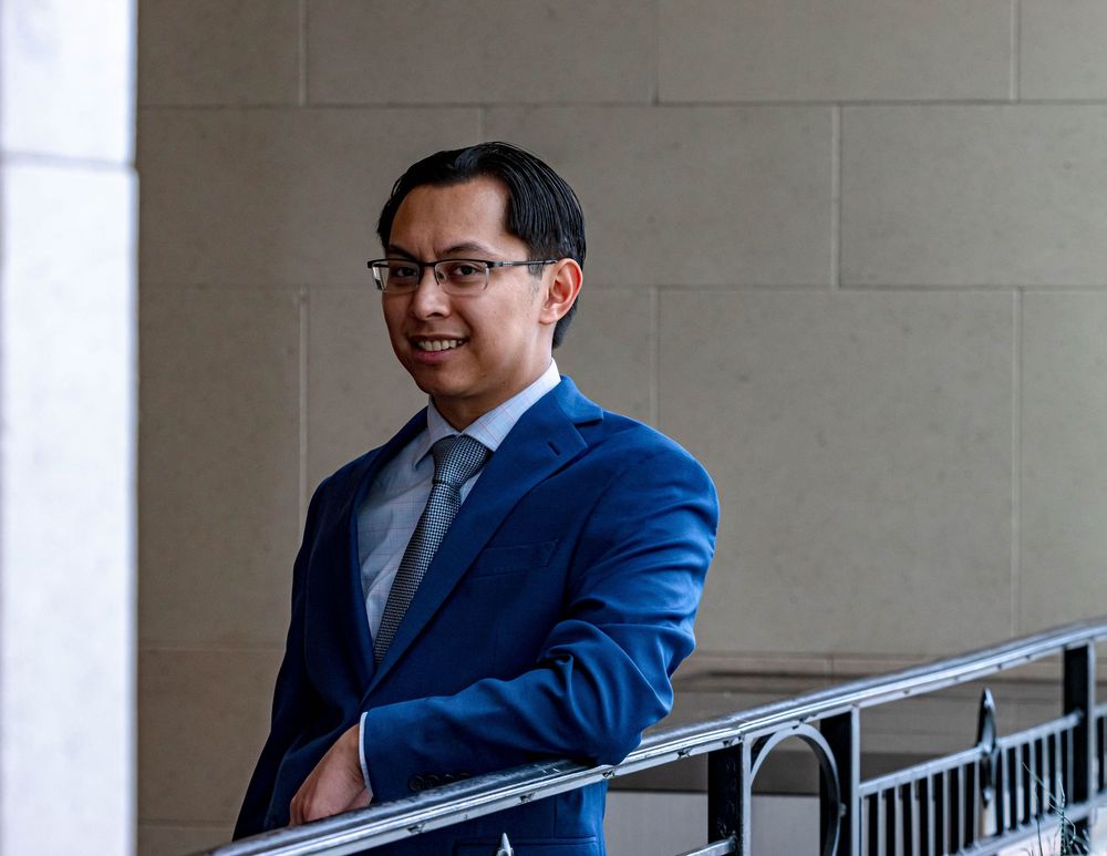 Professional in a royal blue suit smiling while standing next to a railing in a building interior.