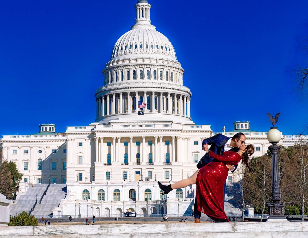 Tourist wearing red jacket poses for photo in front of the United States Capitol Building dome on a sunny day.