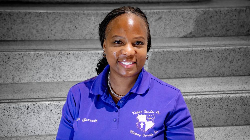 A medical professional in a purple polo uniform sitting on gray stone steps outdoors.