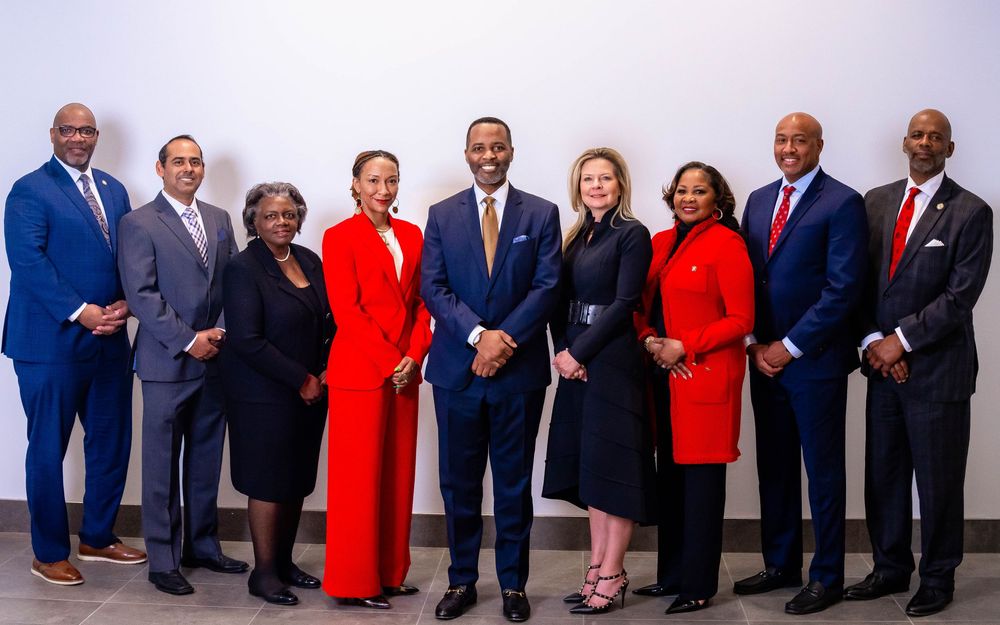 A professional group photo of executives in formal business attire standing together against a light background.