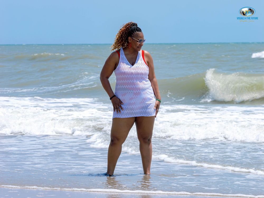 Someone enjoys a summer day standing in the ocean waves at the beach wearing a white tank top.