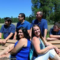 Group of six people posing on wooden platform near lake in blue outfits.