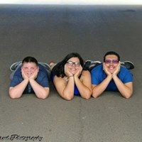 Three siblings lying on ground smiling wearing blue coordinating outfits.