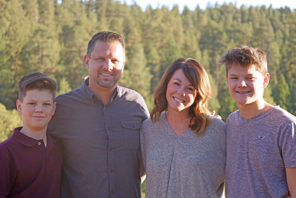 Cheerful family of four smiling together outdoors with pine forest in the background.