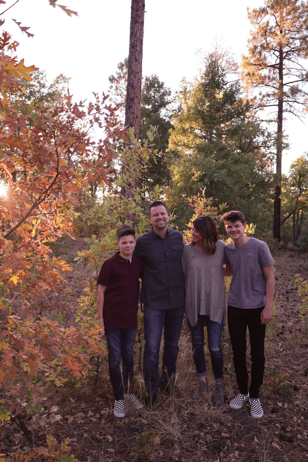 Family of four posing in autumn forest with colorful fall foliage at sunset.