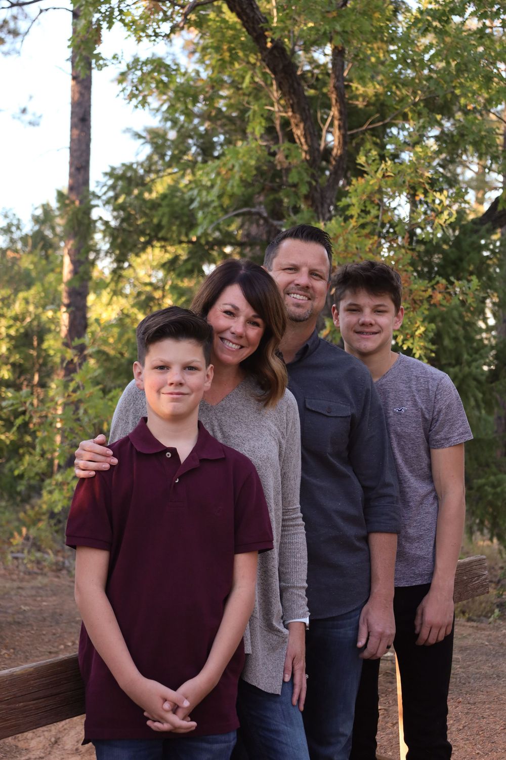 Smiling family of four posing together in a wooded outdoor setting with pine trees.