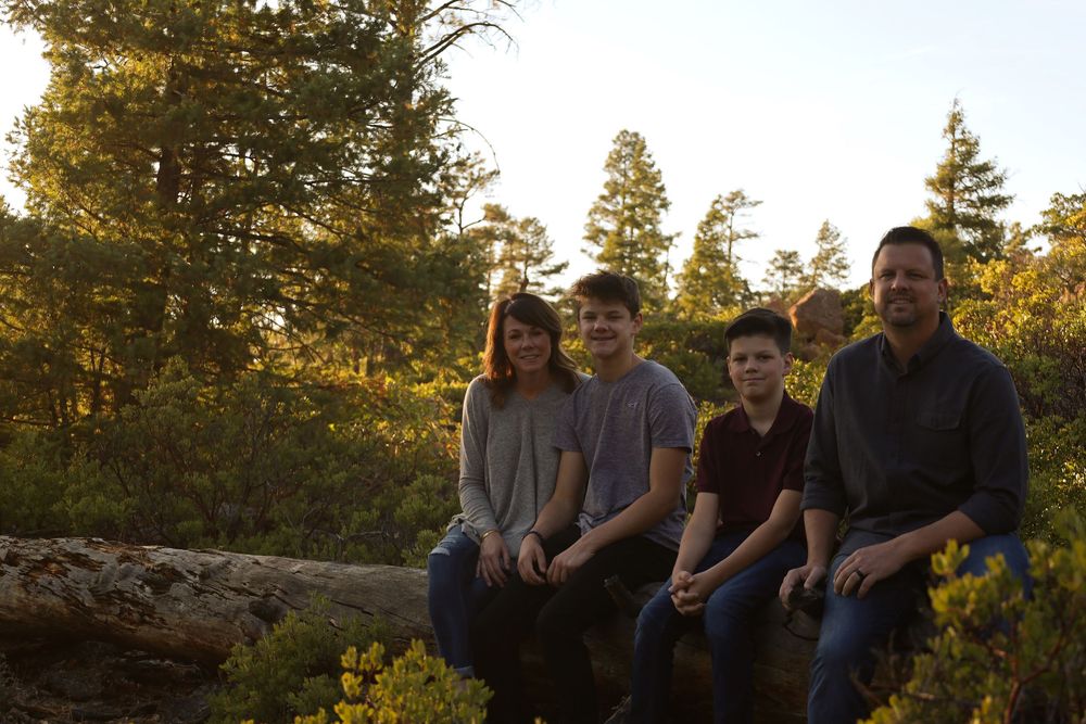 Family of four sitting on a log in a forest during golden hour sunset.