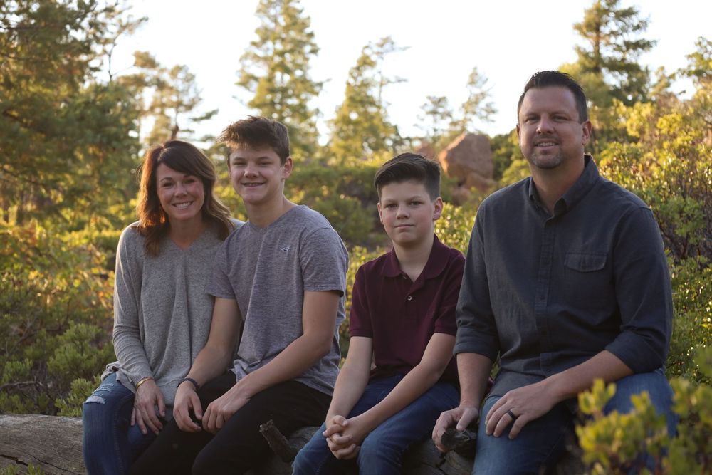 Family of four sitting together on rocks surrounded by lush green forest scenery.