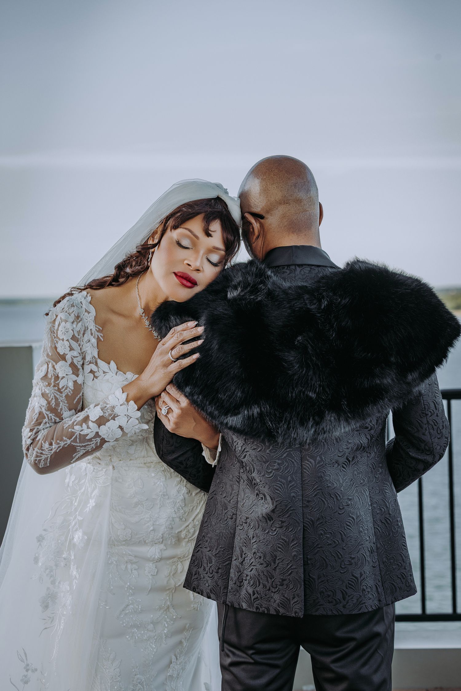 A couple shares an intimate moment during their wedding, with the bride in lace and the groom in a dark suit.