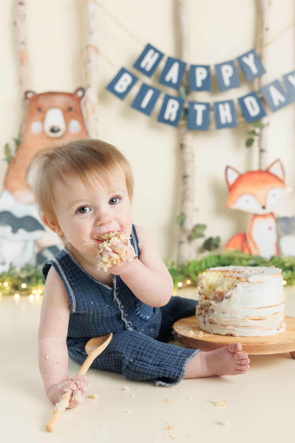 Small child enjoying birthday cake in a woodland-themed party setup with bear and fox decorations.