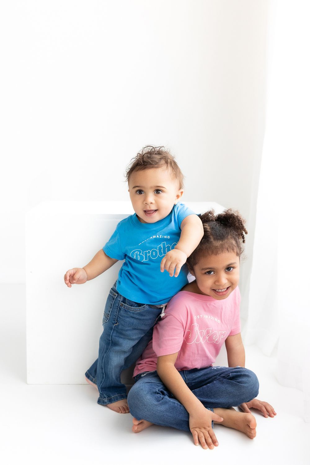Two children in casual clothing play and pose together against a white background.
