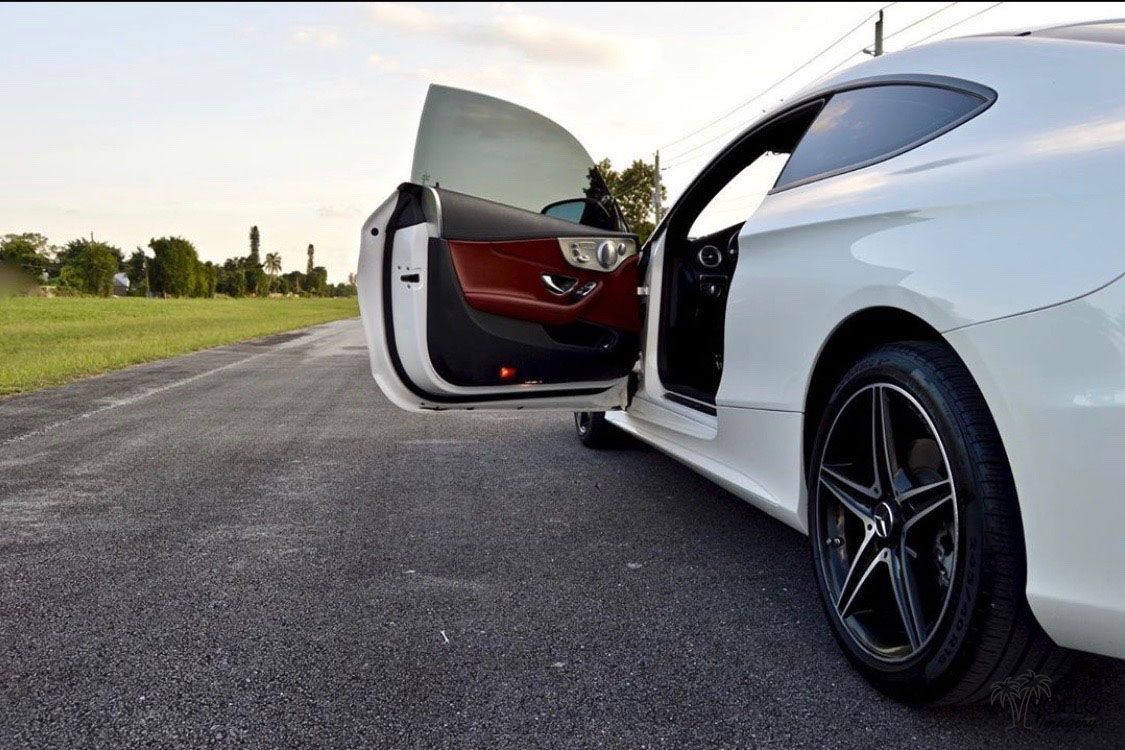 White sports car with open door showing red interior on an empty road.