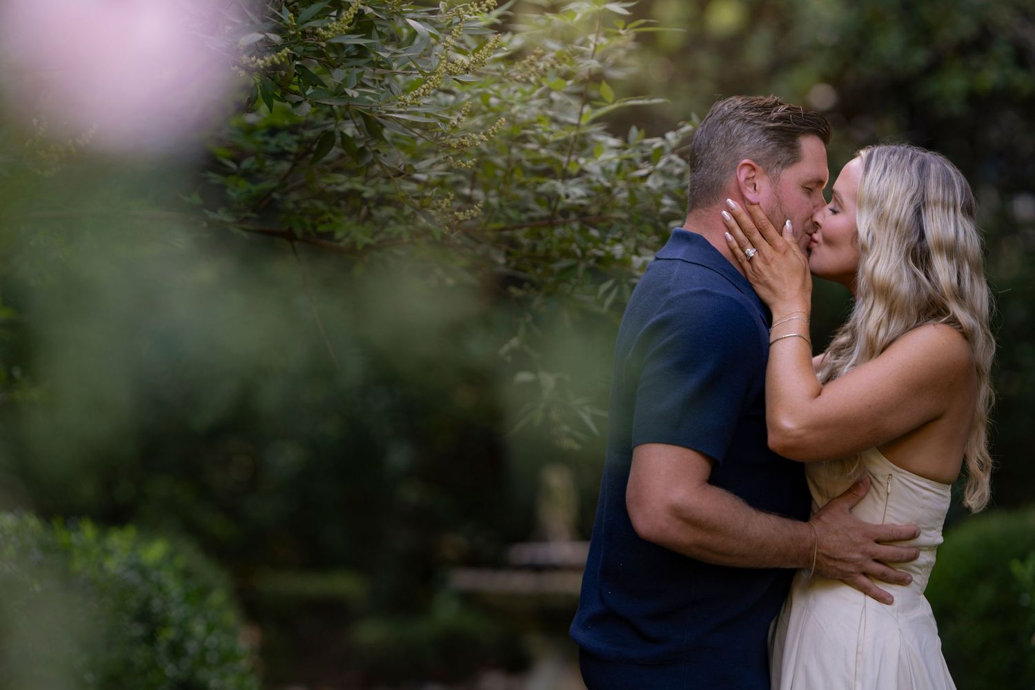 A romantic couple shares an intimate kiss in a lush garden setting during a photo session.