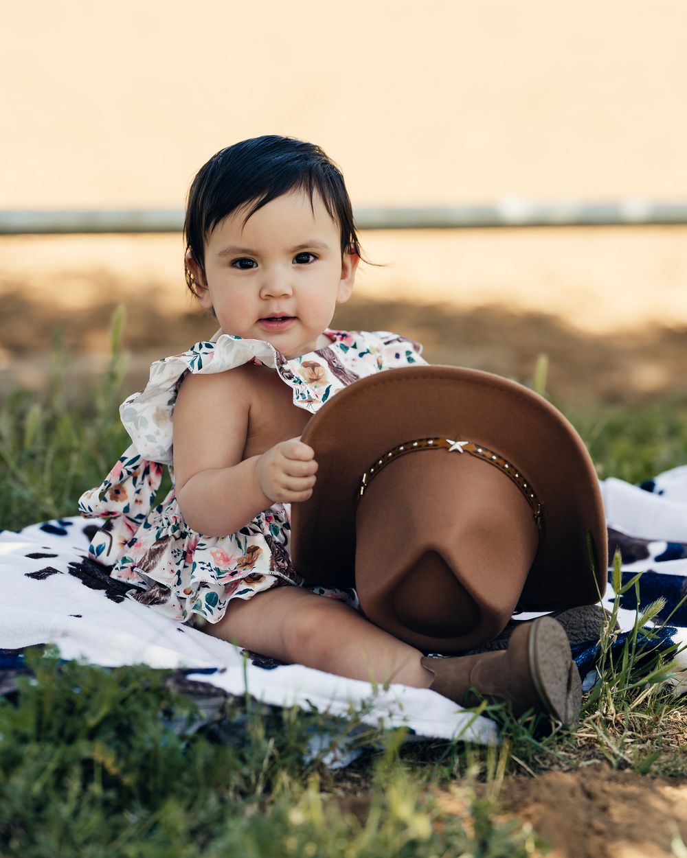A tiny cowgirl outfit and hat are displayed on a white blanket in an outdoor setting.