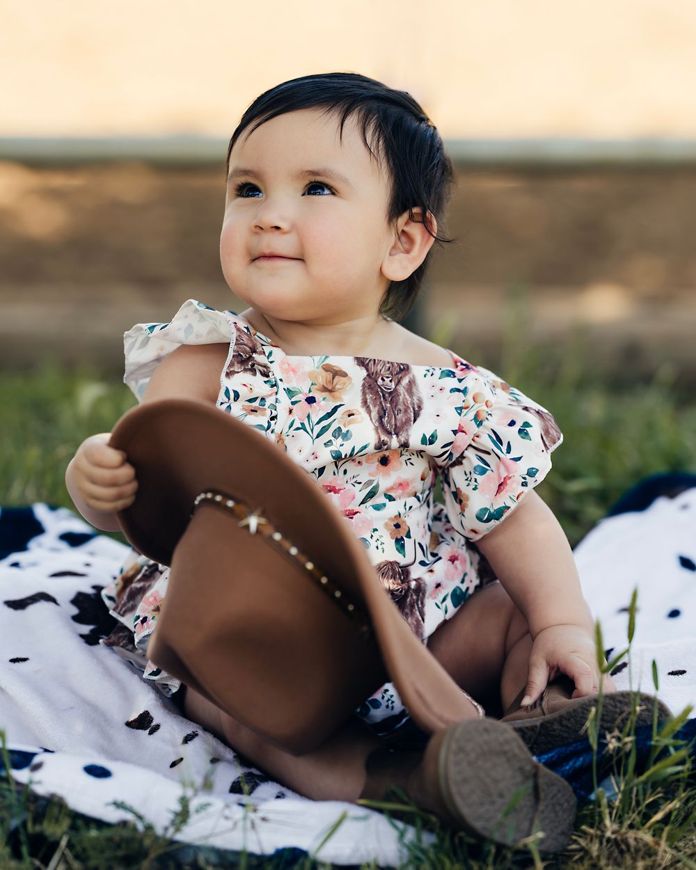 A floral romper and brown cowboy hat create a western-themed scene on grass.