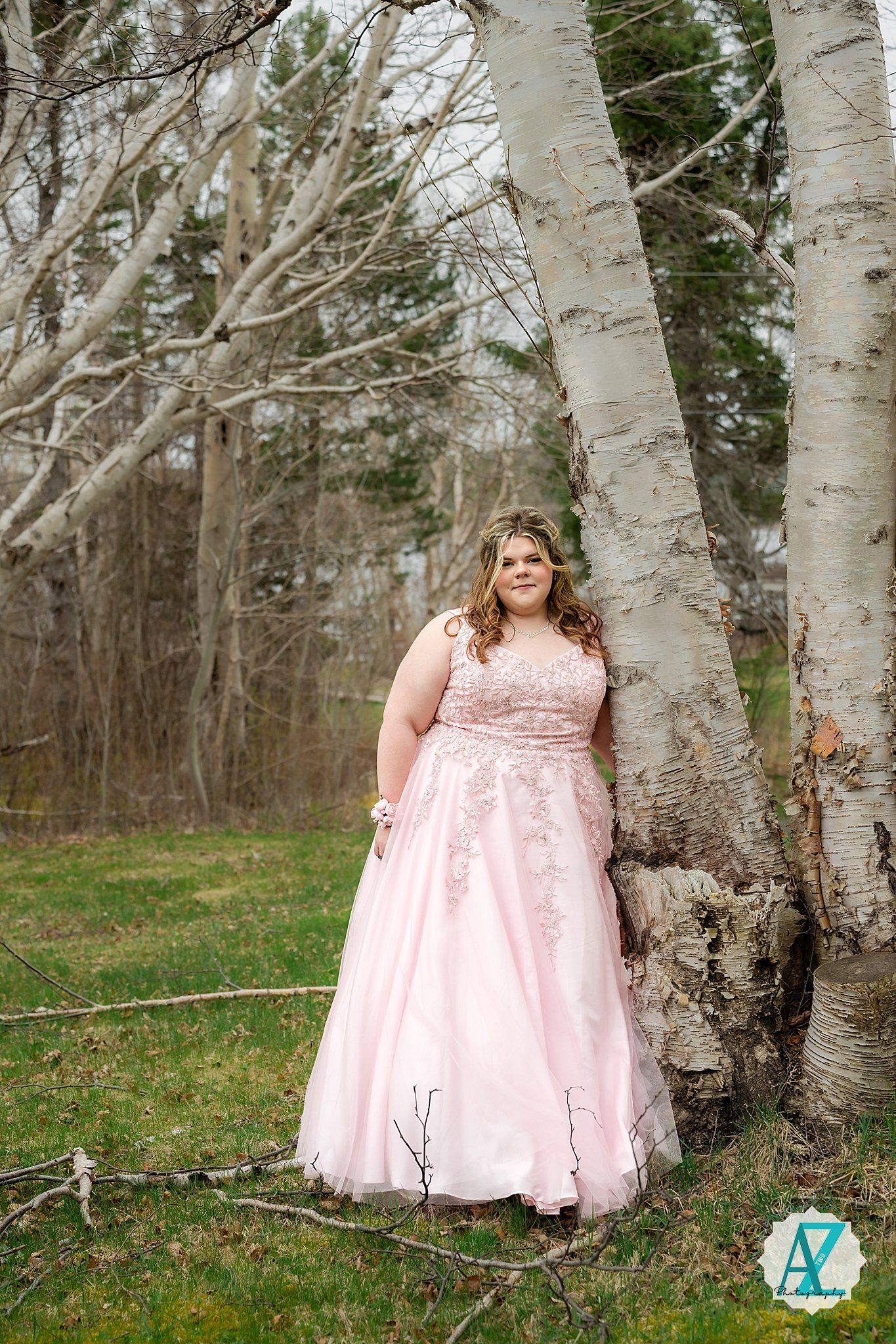A person in a flowing pink gown stands elegantly among birch trees in a springtime forest setting.