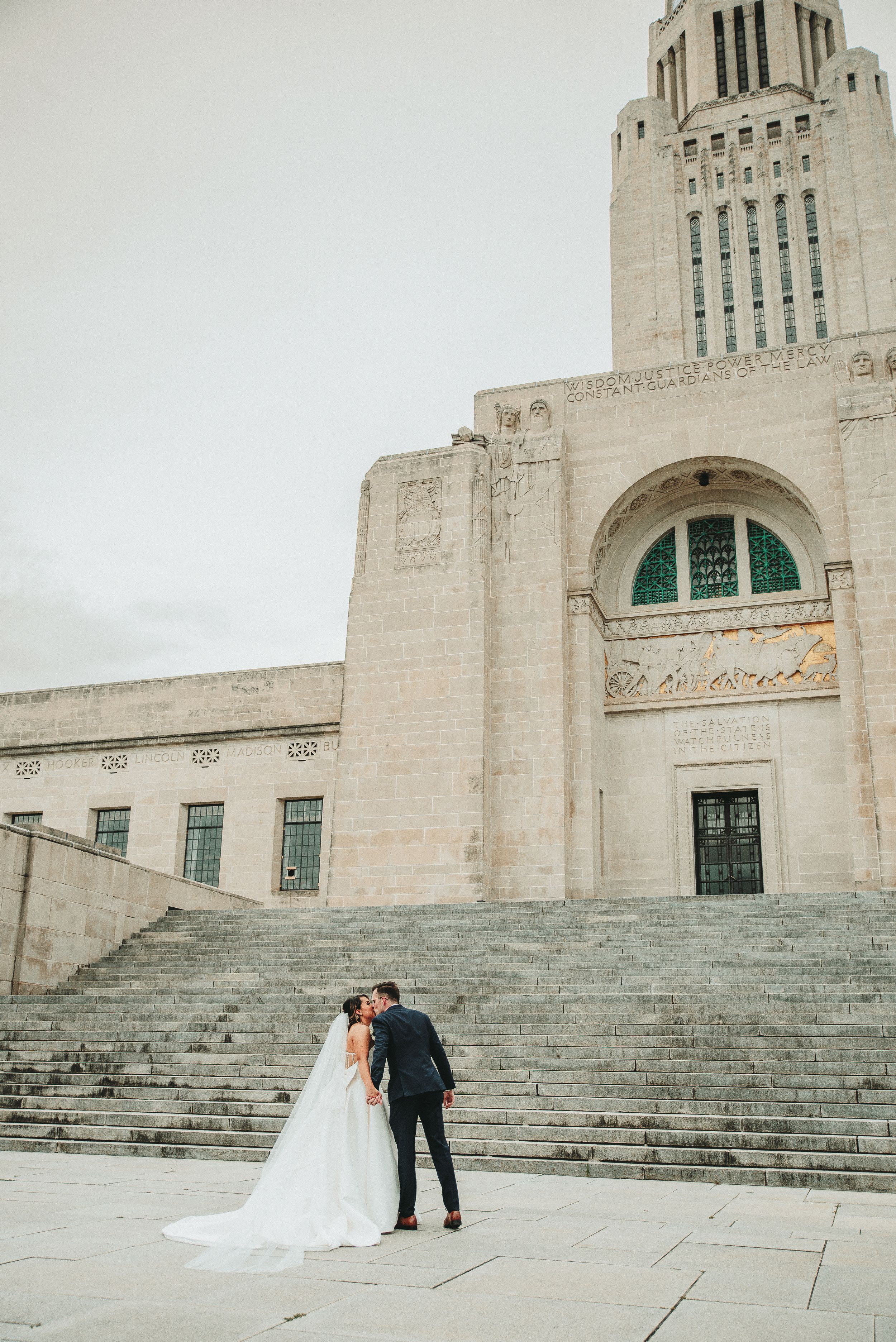 A wedding couple poses on the dramatic stone steps of a historic building.