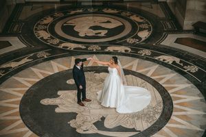 A wedding couple stands on an intricate circular floor pattern inside a grand building.