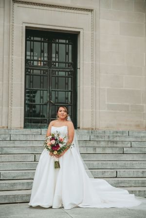 A bride in a flowing white gown poses on stone steps with a colorful bouquet.