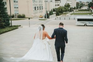 A couple walks along a modern urban plaza outside a stone building.