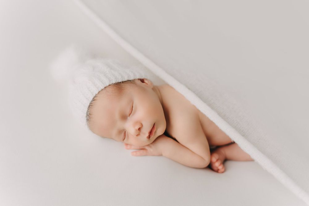 A sleeping newborn baby curled up peacefully under soft white fabric.