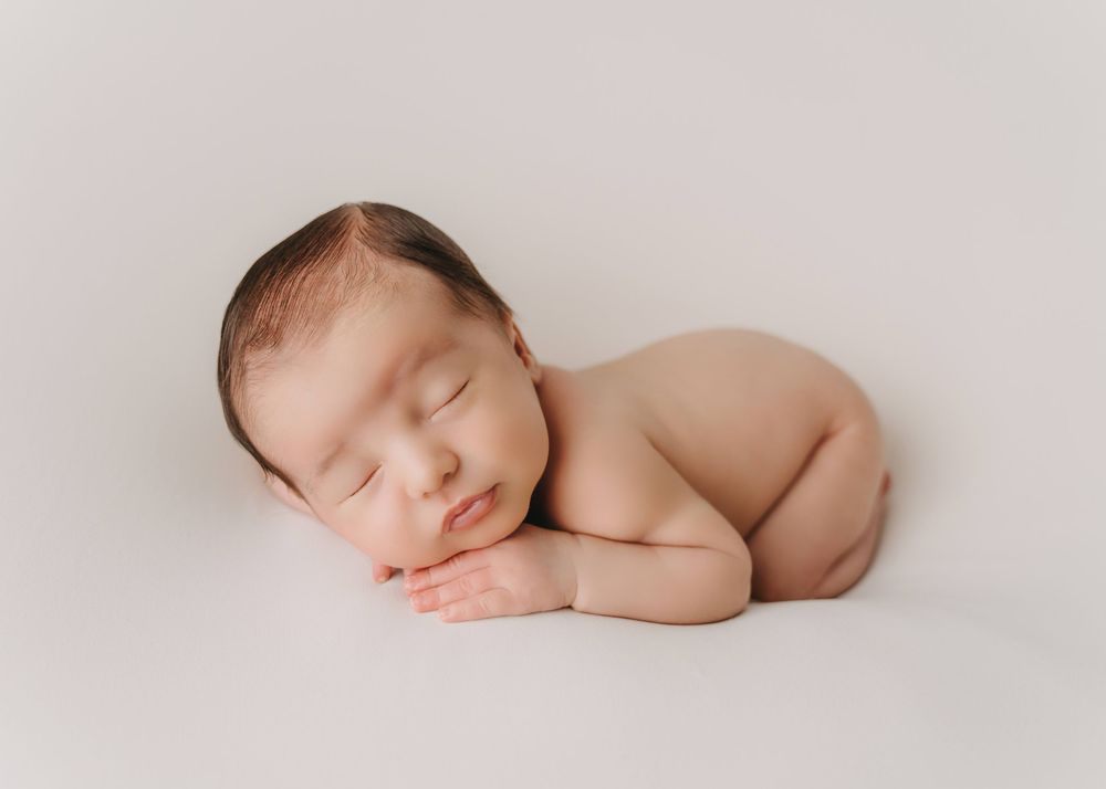 Peaceful sleeping newborn baby posed on soft cream backdrop in minimalist style photography.