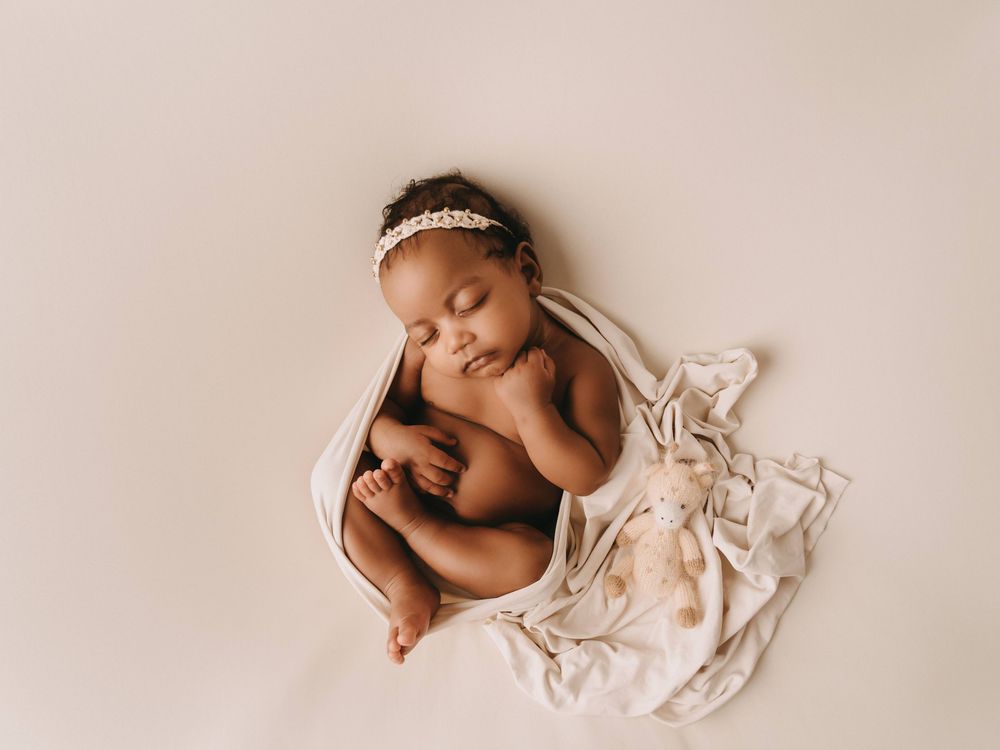 Sleeping newborn resting on soft white fabric wearing delicate headband during professional photography shoot.