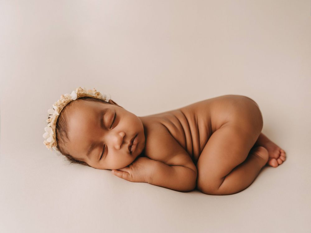 Peaceful sleeping newborn baby wearing a delicate pearl headband laying on soft beige background in studio lighting.