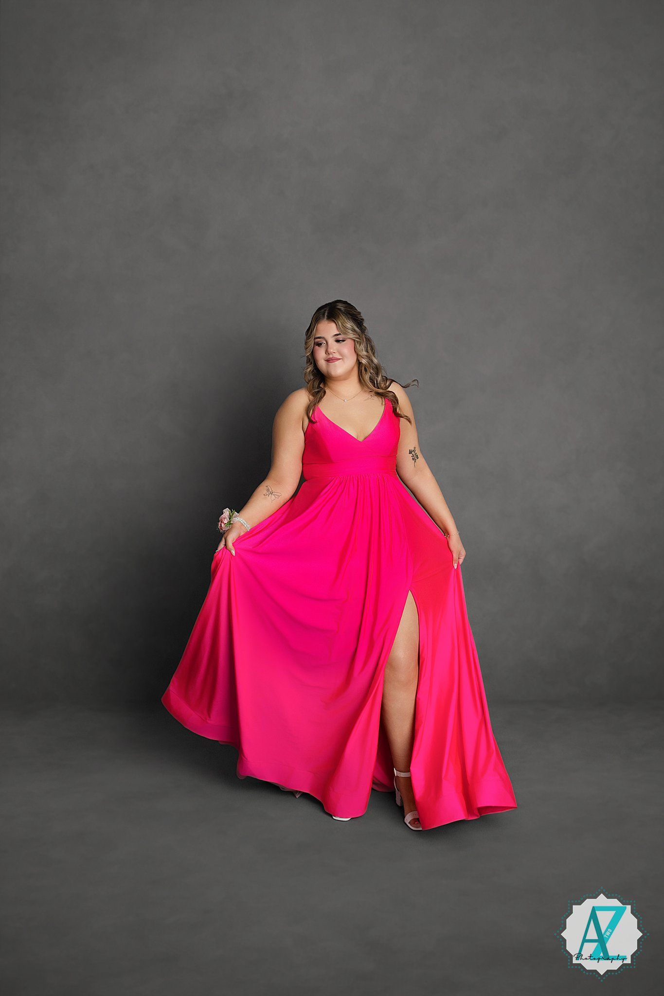Stunning hot pink floor-length formal gown with v-neck and high slit showcased against grey studio backdrop.
