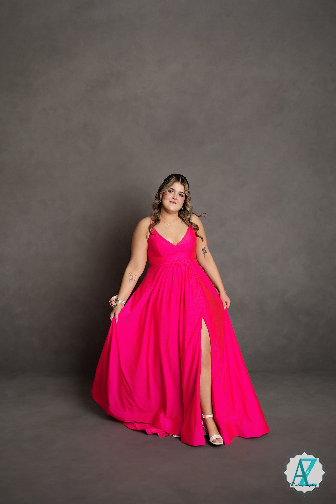 Elegant pink flowy evening gown with high slit and v-neckline modeled in studio setting.