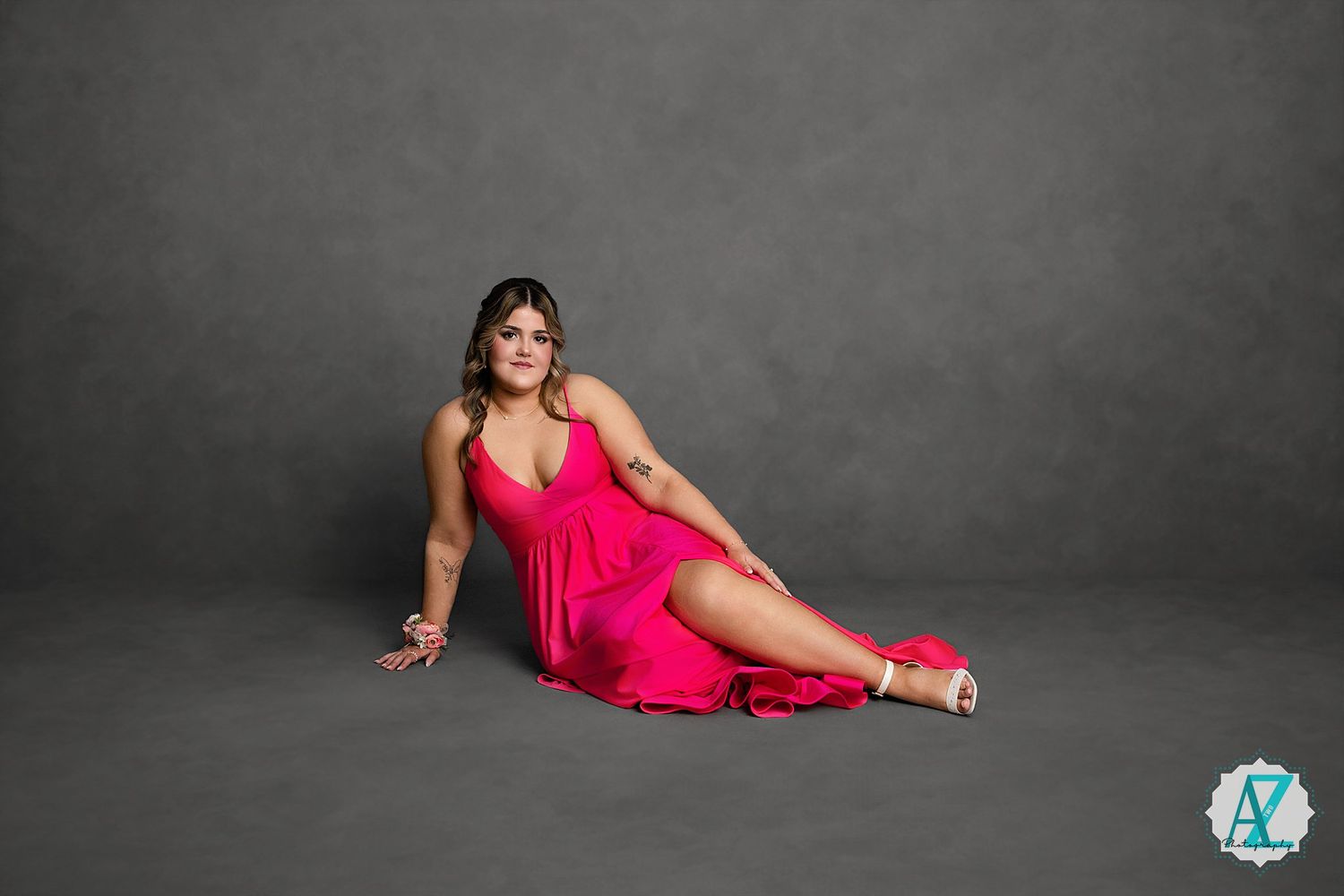 A woman in a vibrant red dress poses elegantly on a gray studio floor.
