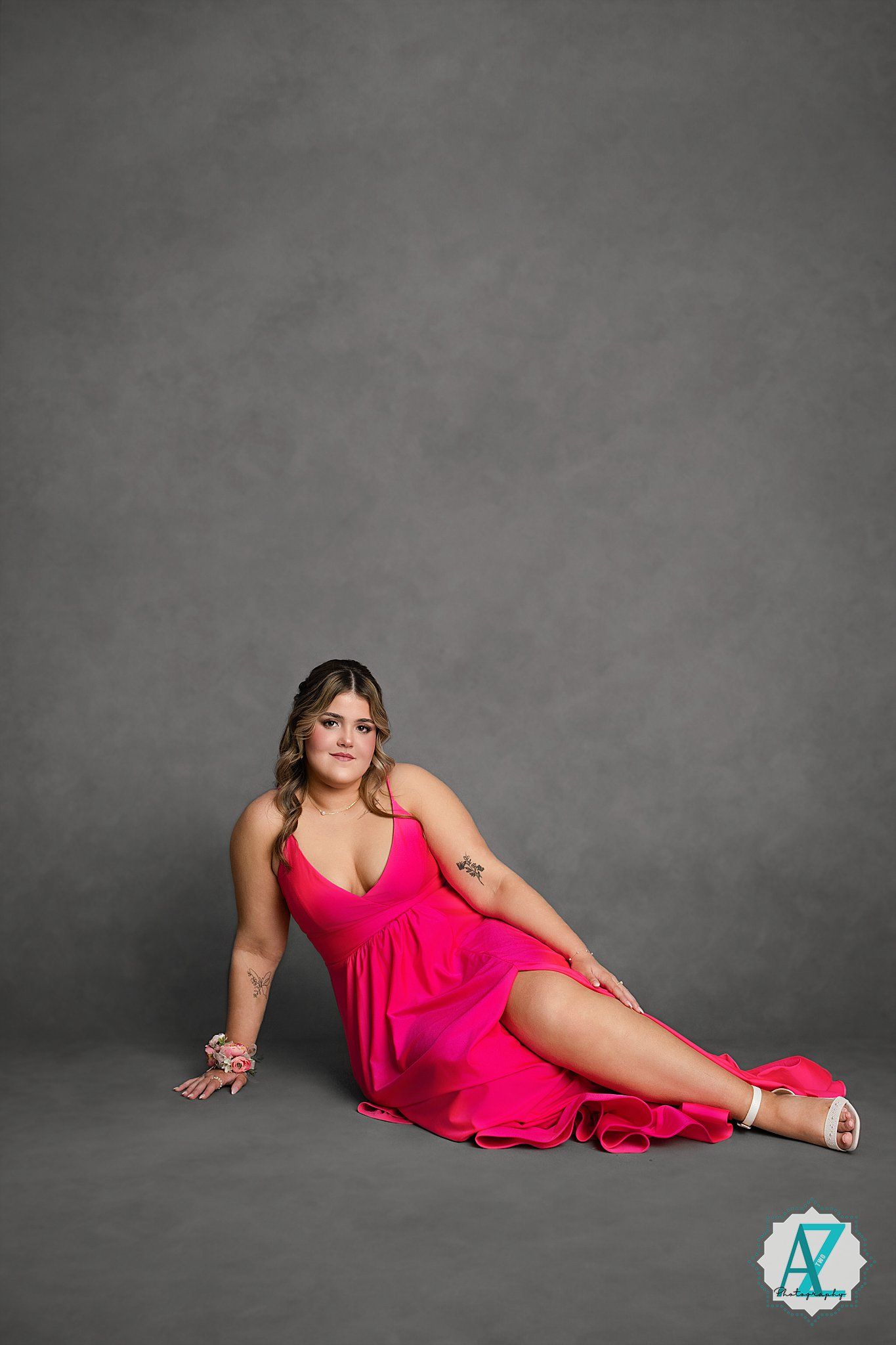 Glamorous pink gown photographed in reclining pose against grey backdrop.