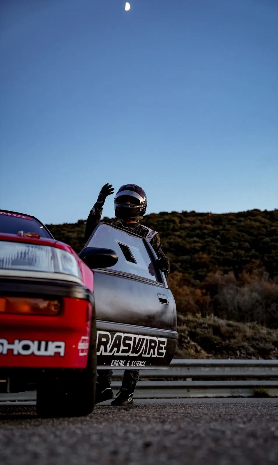 Un homme en combinaison de course est assis à l’arrière d’une voiture de rallye blanche et rouge, prêt pour le départ.
