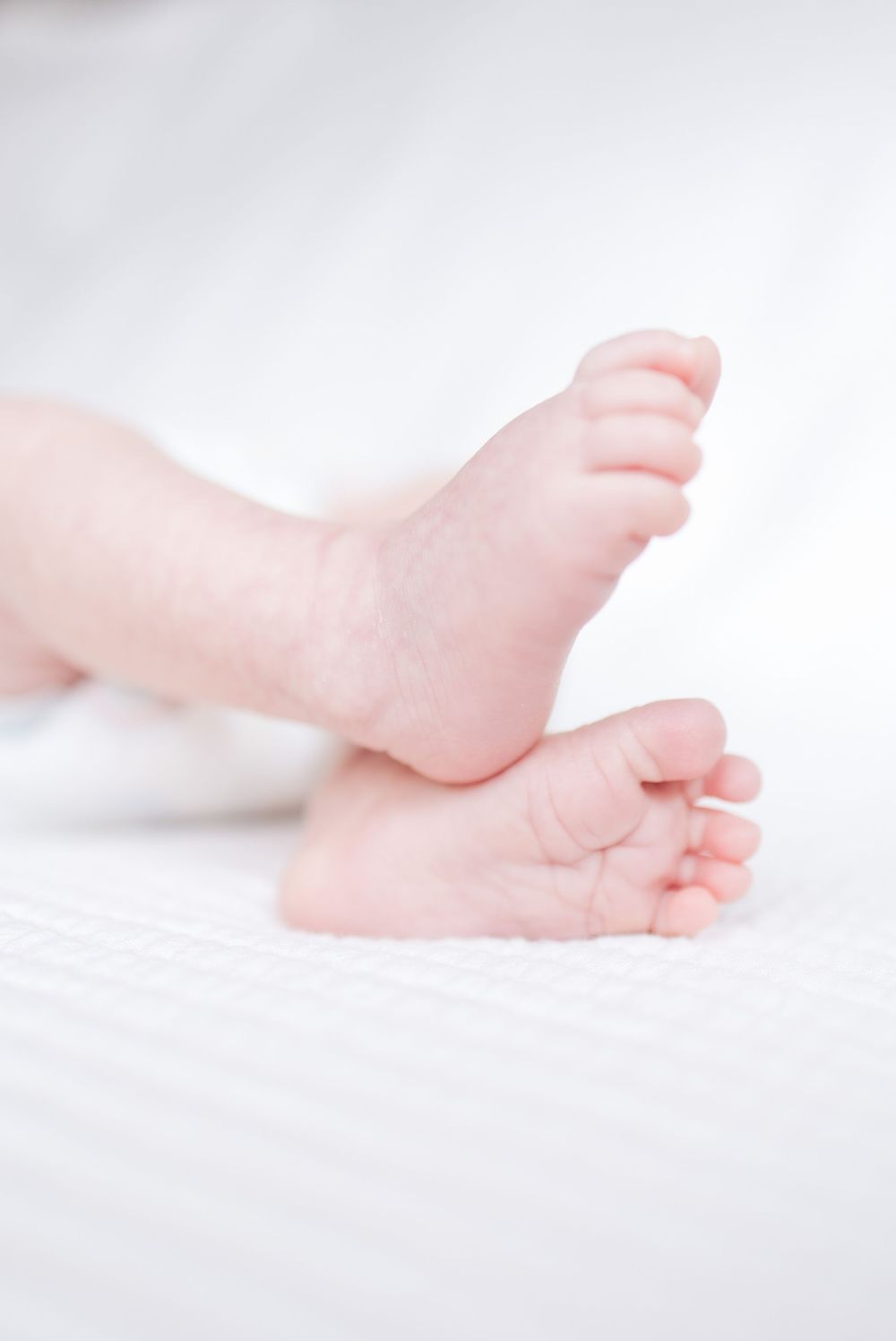 Close-up of tiny baby feet resting on soft white bedding in natural lighting.