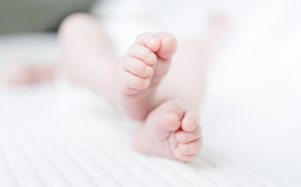 Tiny newborn baby feet with curled toes resting on soft white fabric in dreamy high-key lighting.