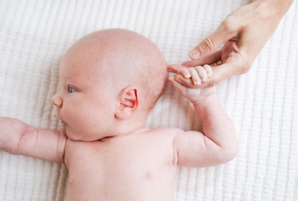 A gentle hand touches a newborn baby lying on white textured bedding.