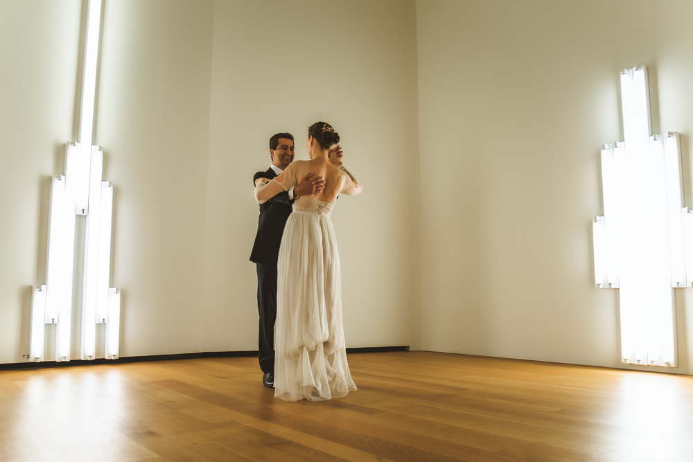A couple shares their first dance in an elegant minimalist room with white walls and warm wooden floors.