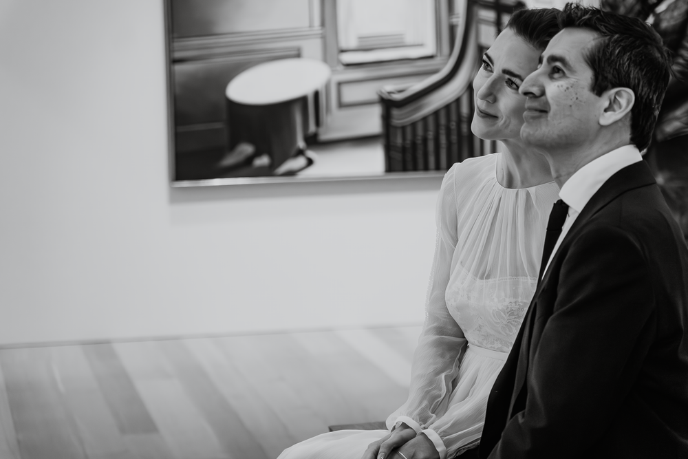 A couple sits together indoors looking up in contemplation during what appears to be a quiet moment in black and white.