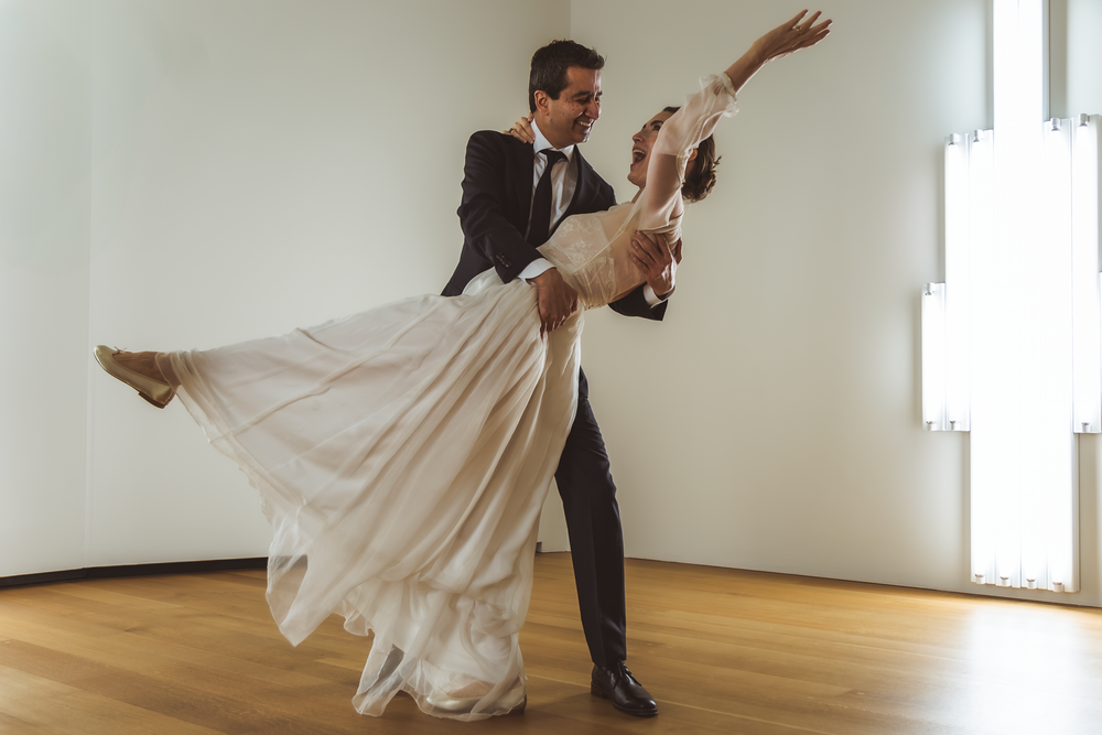 A couple performs an elegant dance dip move on a wooden floor in formal attire.