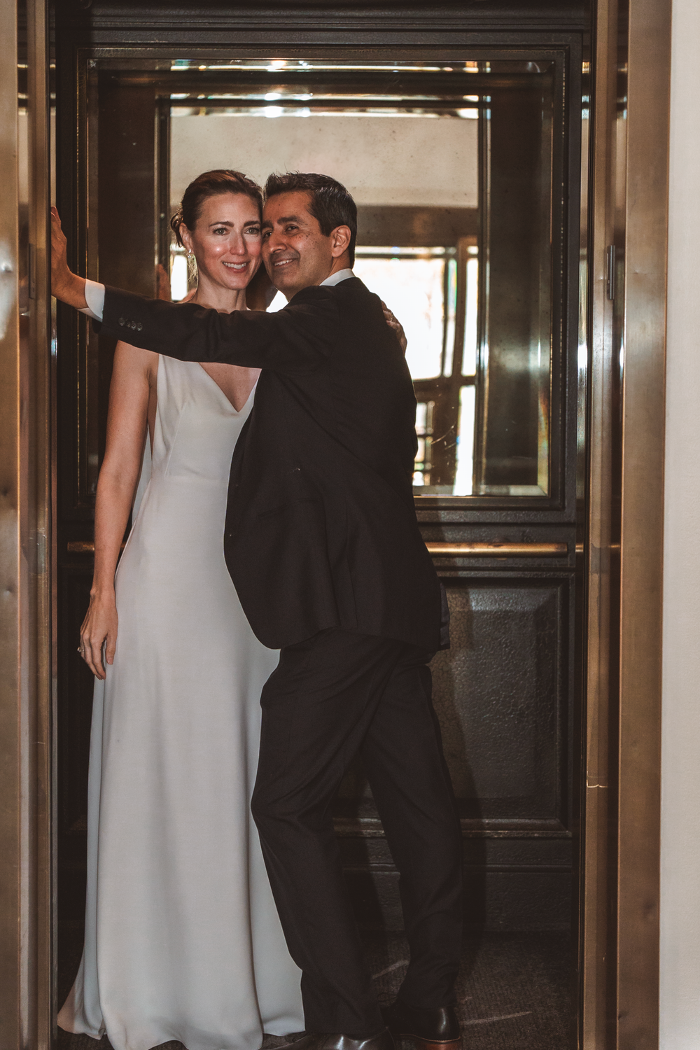 Elegant couple in formal attire share a tender moment while entering a revolving door together.