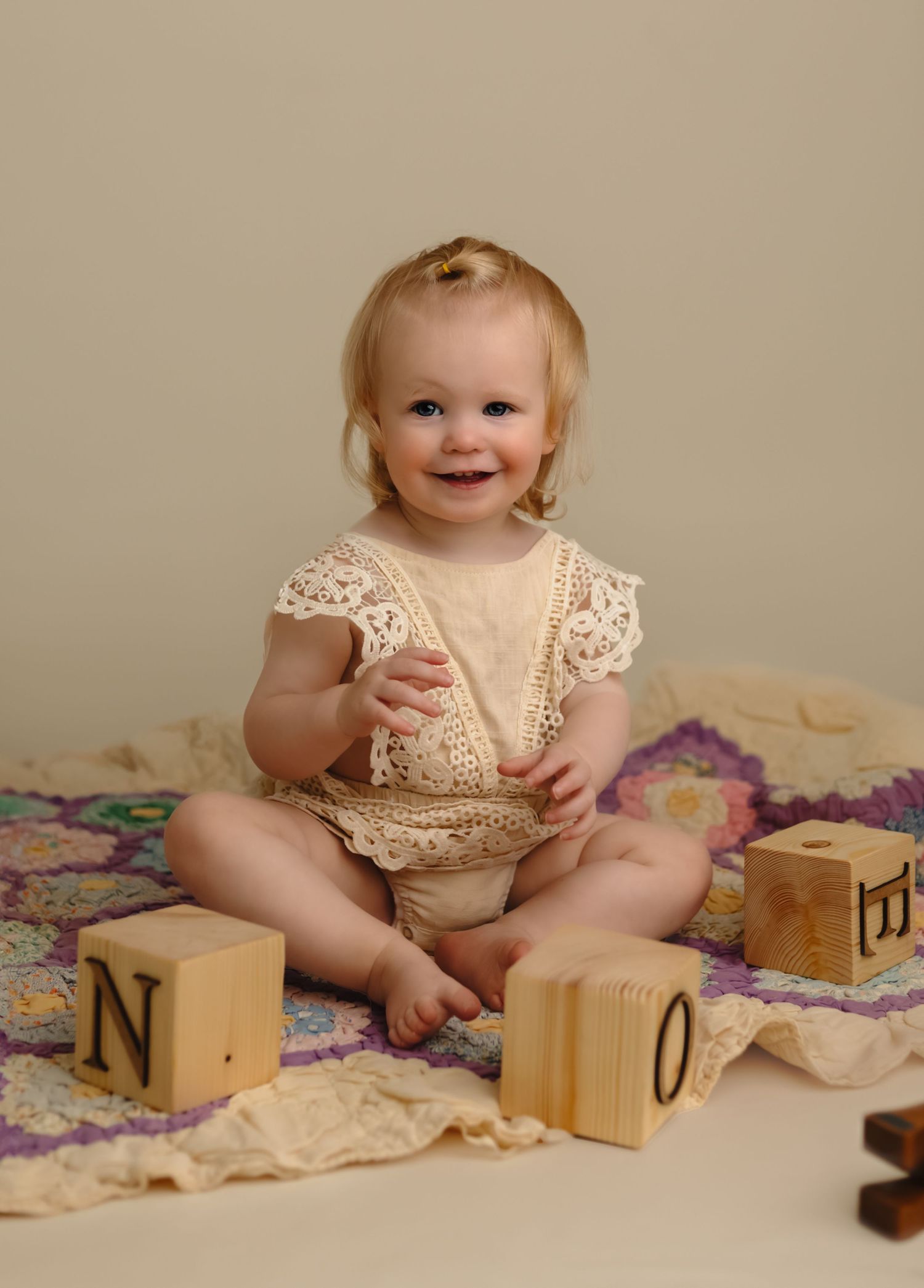 Smiling baby girl playing with alphabet blocks and sitting on an heirloom pink and purple quilt  in Charlottesville newborn studio.