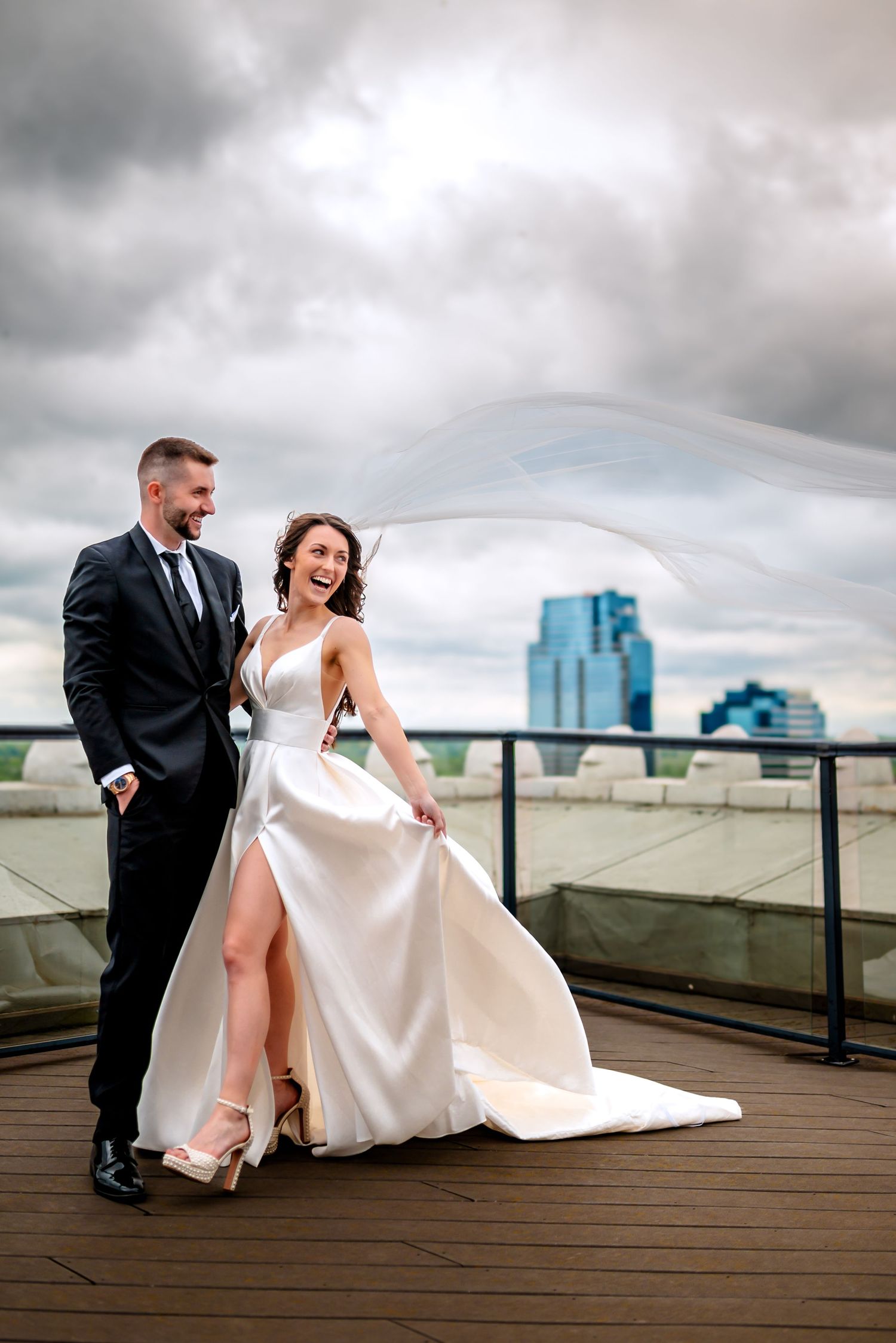 A tender intimate moment between newlyweds sharing a kiss outdoors with dramatic cloudy skies and flowing veil in the wind Grand Rapids