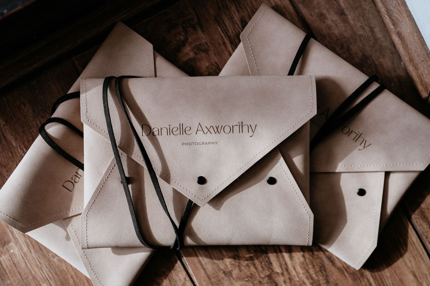 Leather envelopes with Mollie Axworthy branding stacked together on wooden surface.