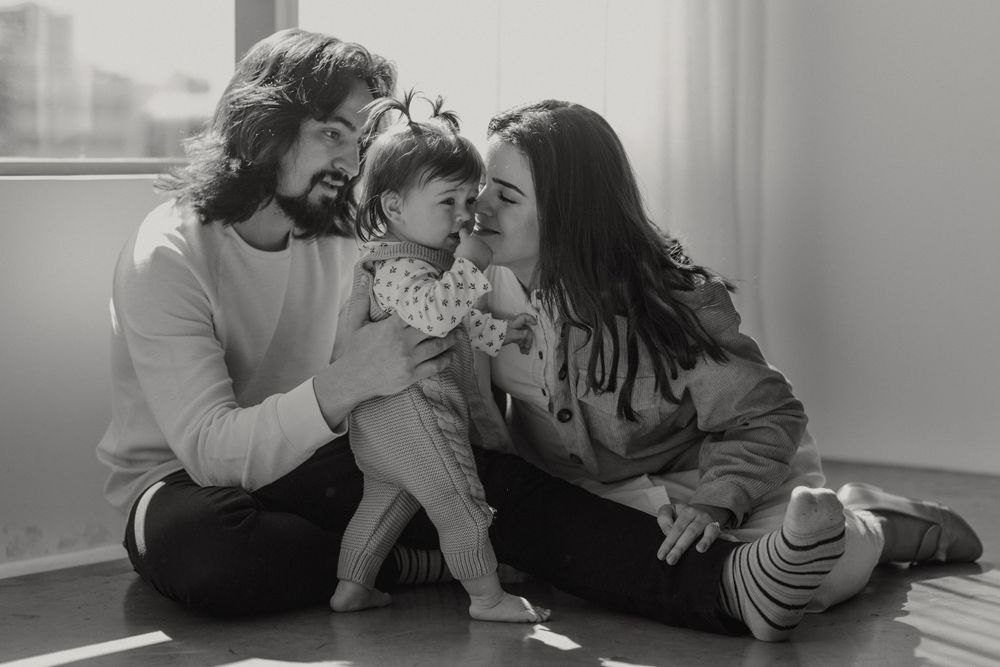 A loving family shares a tender moment together while sitting on the floor near a window in black and white.
