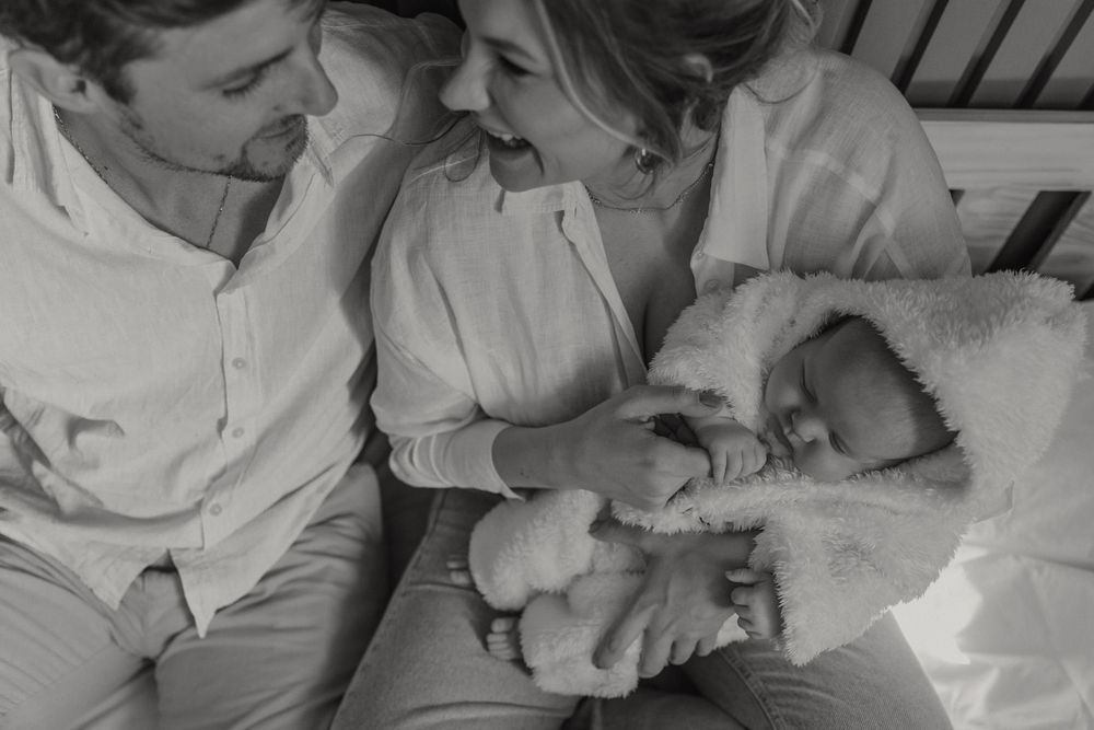 A tender black and white photograph of parents gazing lovingly at their newborn baby wrapped in blankets.