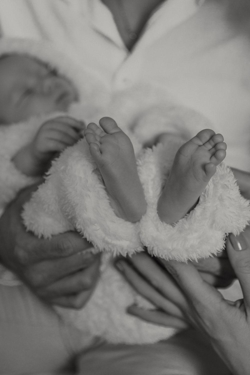 Close up black and white photo of tiny baby feet resting on soft white blanket or fabric.